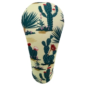 May include: A beige fabric golf headcover with a cactus print. The cactus is green with red flowers. The headcover is shaped like a golf club head.