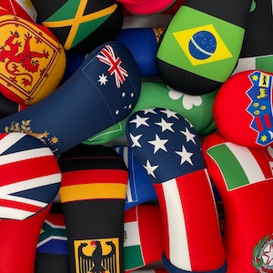 Puede incluir: Una colección de fundas para palos de golf de colores con diferentes banderas y diseños, incluyendo la bandera estadounidense, la bandera jamaicana, la bandera brasileña y la bandera australiana.