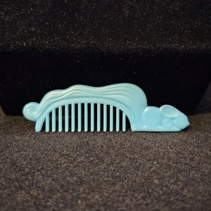 May include: A light blue plastic comb shaped like a mouse. The comb has a wavy design on top and a mouse head on the end.