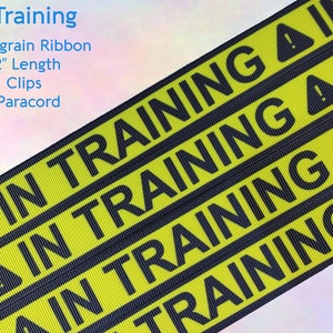 May include: Yellow and black grosgrain ribbon with the text "IN TRAINING" repeated multiple times. The ribbon also features a black triangle with an exclamation point inside. The text "KAM Clips", "9" - 12" Length", "Grosgrain Ribbon", "In Training", and "550 Paracord" are also visible.