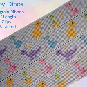 May include: White grosgrain ribbon with a repeating pattern of colorful baby dinosaurs. The ribbon is 9-12 inches long and includes KAM clips and 550 paracord.