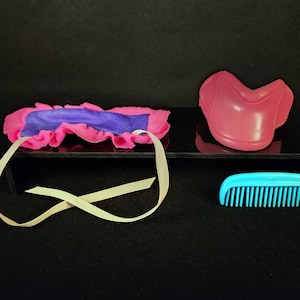 May include: A set of three pink and blue plastic horse grooming tools. The set includes a pink saddle, a pink and purple mane comb, and a blue comb.