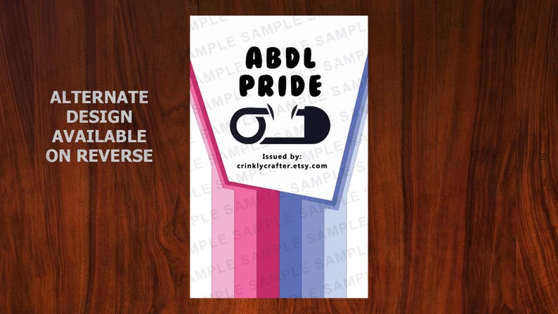 K&ouml;nnte beinhalten: Ein wei&szlig;es rechteckiges Design mit den schwarzen Worten "ABDL PRIDE" und einer Grafik einer Windel-Sicherheitsnadel. Das Design hat rosa und blaue Streifen und den Text "ALTERNATE DESIGN AVAILABLE ON REVERSE". Der Etsy-Shop ist crinklycrafter.etsy.com.