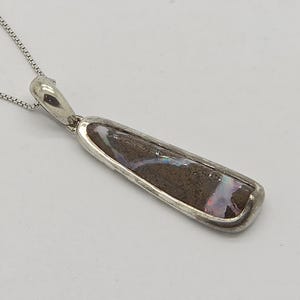 May include: A silver necklace with a rectangular pendant. The pendant features a dark brown stone with white and purple inclusions, set in a silver bezel. The chain is a delicate silver box chain.
