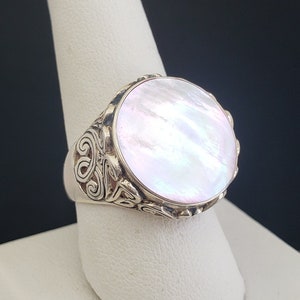 May include: A silver ring with a large, round, white mother-of-pearl stone set in a detailed, ornate design.
