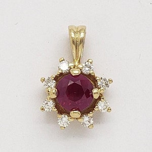 Könnte beinhalten: Ein goldener Anhänger mit einem runden Rubin-Edelstein, der von einem Heiligenschein aus kleineren Diamanten umgeben ist.
