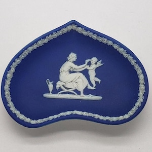 Könnte beinhalten: Eine blaue und weiße herzförmige Keramikschale mit einem erhabenen weißen Design einer Frau und eines Kindes. Die Schale ist mit einem weißen floralen Rand verziert.