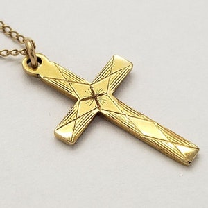 May include: A gold chain necklace with a gold cross pendant. The cross has a geometric design with a star in the center.