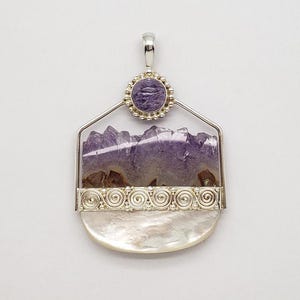 Peut inclure: Pendentif en argent avec une grande améthyste violette irrégulière. Le pendentif a une forme géométrique avec une bordure décorative en argent et une petite pierre violette en haut. Sur fond blanc.