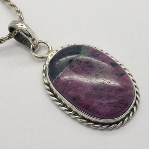 May include: A silver chain necklace with a pendant featuring a pink and green oval gemstone set in a silver bezel with a rope-like border.