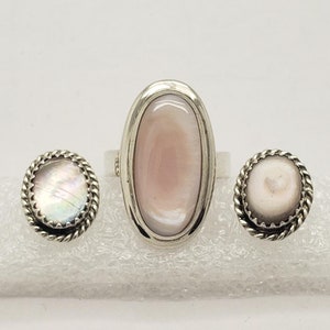 May include: A set of three silver rings with oval-shaped mother-of-pearl stones. The ring is larger than the earrings.
