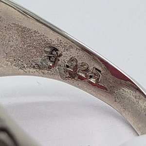 May include: Close-up of the inside of a silver ring with the number "925" stamped on the band.