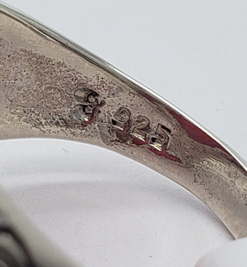 May include: Close-up of the inside of a silver ring with the number "925" stamped on the band.