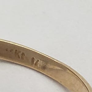 May include: Close-up of a gold ring with a textured band. The ring is stamped with "14K" and "04" on the inside of the band. The ring is set against a white background.