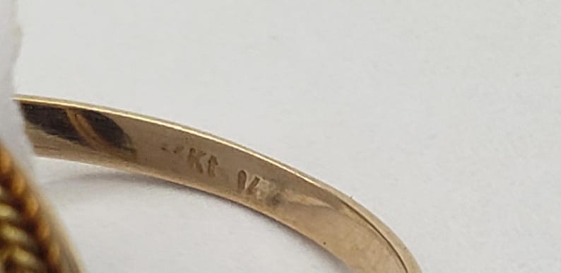May include: Close-up of a gold ring with a textured band. The ring is stamped with "14K" and "04" on the inside of the band. The ring is set against a white background.