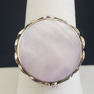 May include: A ring with a large, round, white mother-of-pearl stone set in a gold-toned metal band.