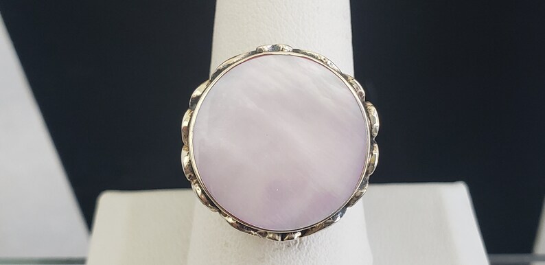 May include: A ring with a large, round, white mother-of-pearl stone set in a gold-toned metal band.