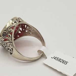 May include: A silver ring with a red stone set in a filigree design. The ring is on a white background with a tag that says "J458265".