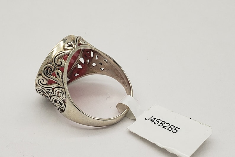 May include: A silver ring with a red stone set in a filigree design. The ring is on a white background with a tag that says "J458265".