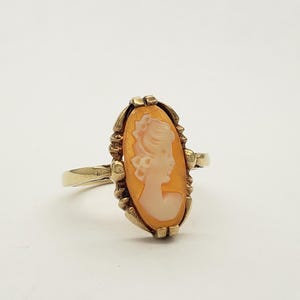 May include: Gold ring with a cameo featuring a woman's profile in a white cameo set in a gold oval frame.