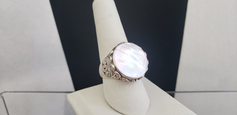 May include: A silver ring with a large, round, white mother-of-pearl stone set in a detailed, ornate design.