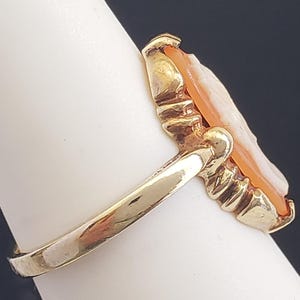 May include: A gold ring with a cameo setting. The cameo is carved from shell and features a portrait of a woman. The ring is set on a white background.
