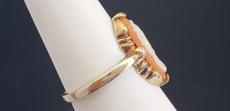 May include: A gold ring with a cameo setting. The cameo is carved from shell and features a portrait of a woman. The ring is set on a white background.