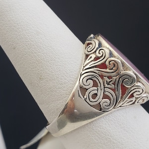 May include: A silver ring with an oval-shaped, dark purple gemstone set in a filigree design.