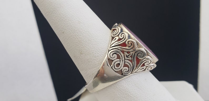 May include: A silver ring with an oval-shaped, dark purple gemstone set in a filigree design.