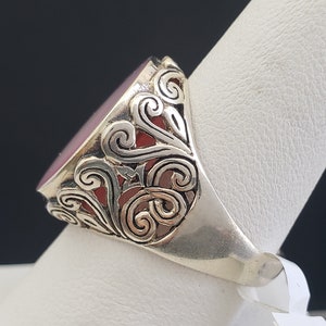 May include: A silver ring with a red gemstone set in a filigree design.