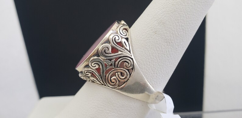 May include: A silver ring with a red gemstone set in a filigree design.
