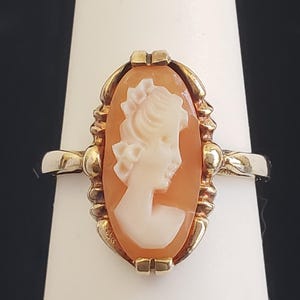May include: A gold ring with a cameo featuring a woman's profile in white against a peach background.