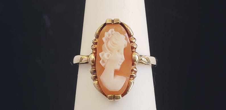 May include: A gold ring with a cameo featuring a woman's profile in white against a peach background.