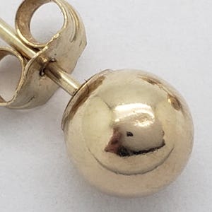 Pu&ograve; includere: Primo piano di un singolo orecchino a sfera d'oro. L'orecchino presenta una sfera rotonda e lucida in oro e un perno con chiusura a farfalla. L'orecchino &egrave; posto su uno sfondo bianco.