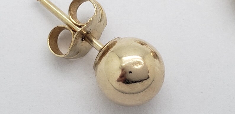 Pu&ograve; includere: Primo piano di un singolo orecchino a sfera d'oro. L'orecchino presenta una sfera rotonda e lucida in oro e un perno con chiusura a farfalla. L'orecchino &egrave; posto su uno sfondo bianco.