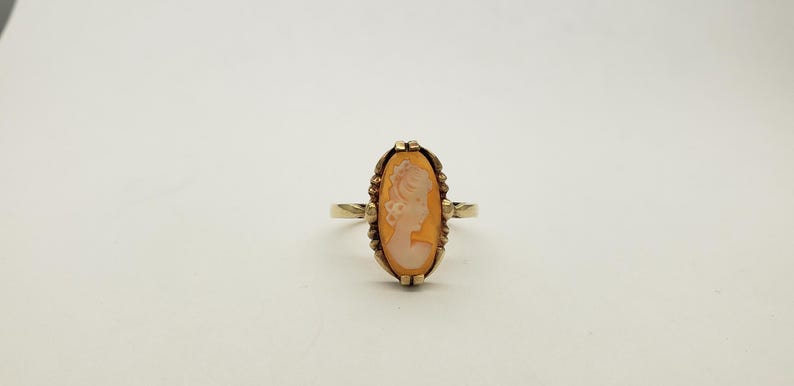 May include: A gold ring with a cameo of a woman's profile set in a oval shaped frame.