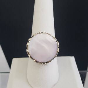 May include: A ring with a large, round, white mother-of-pearl stone set in a gold-toned metal band.