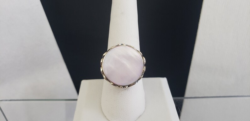May include: A ring with a large, round, white mother-of-pearl stone set in a gold-toned metal band.