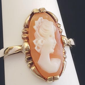 May include: A gold ring with a cameo featuring a woman's profile in white against a peach-colored background.