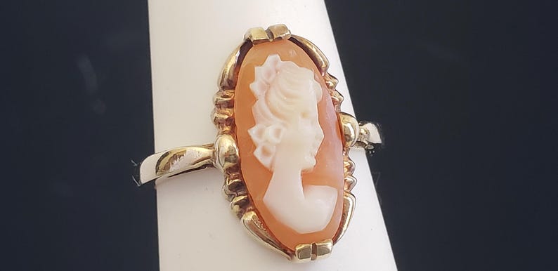 May include: A gold ring with a cameo featuring a woman's profile in white against a peach-colored background.