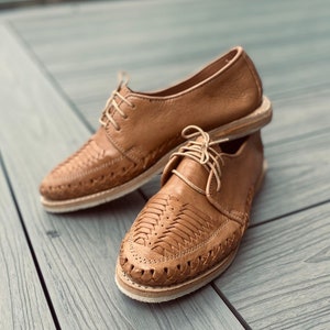 May include: A pair of brown leather shoes with intricate woven designs. The shoes have a lace-up closure and a pointed toe.