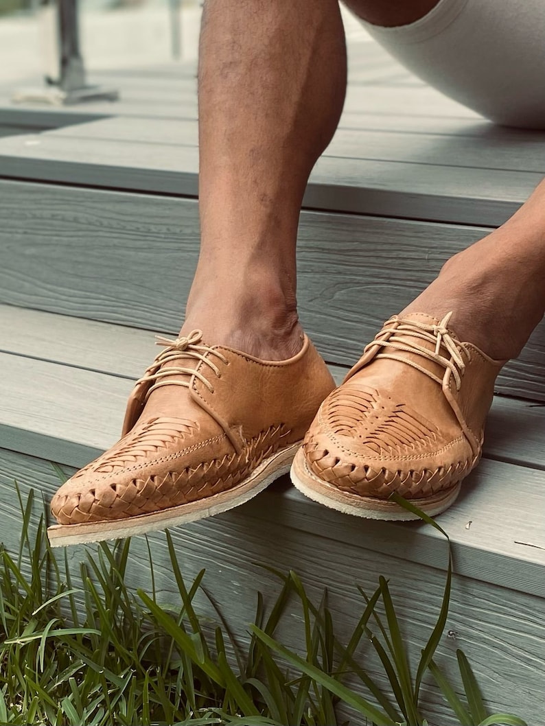 May include: A pair of tan leather shoes with intricate woven designs. The shoes have a lace-up closure and a white sole.