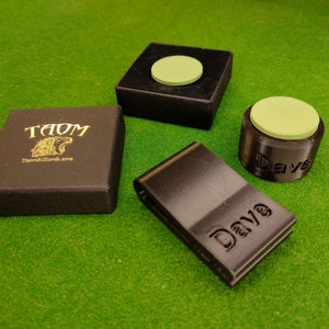 Könnte beinhalten: Vier schwarze Billardkreidehalter mit grüner Kreide. Ein Halter ist eine kleine quadratische Box mit Deckel. Ein weiterer Halter ist ein runder Behälter mit dem Wort "Dave" darauf gedruckt. Der dritte Halter ist eine kleine rechteckige Box mit dem Wort "Dave" darauf gedruckt. Der vierte Halter ist eine kleine rechteckige Box mit den Worten "TAOM" und "Thomsbilliards.com" darauf gedruckt.