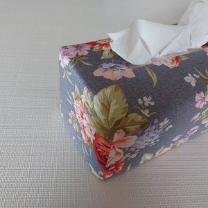 May include: A grey tissue box cover with a floral pattern featuring pink, red, and green flowers. The cover is made of fabric and has a white tissue box inside.