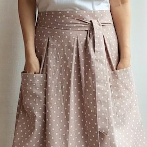 May include: A brown skirt with white polka dots and two pockets. The skirt has a matching fabric belt that ties at the front.