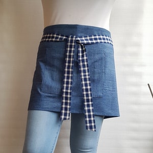 Peut inclure: Un tablier en jean bleu avec un ruban de nouage en vichy blanc et bleu. Le tablier a une seule poche sur le devant.