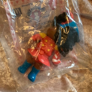 May include: A red and white Happy Meal toy featuring a black-haired character wearing a red and white outfit with a blue hat and blue boots. The toy is packaged in a clear plastic bag with a McDonald's Happy Meal card that says "Congratulations! You're a winner!" and "Happy Meal!"