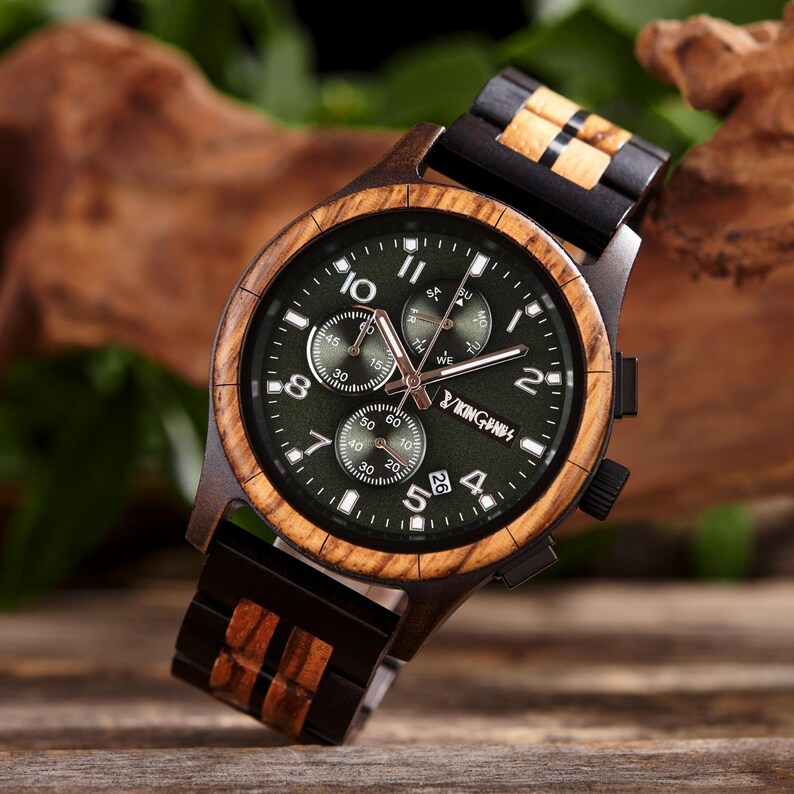 K&ouml;nnte beinhalten: Eine Holzarmbanduhr mit dunkelgr&uuml;nem Zifferblatt und Holzarmband. Das Zifferblatt der Uhr hat wei&szlig;e Ziffern und Hilfszifferbl&auml;tter. Die Uhr hat eine Holzl&uuml;nette und ein dunkelbraunes Armband mit Holzakzenten. Die Uhr hat einen Durchmesser von ca. 4,3 cm.