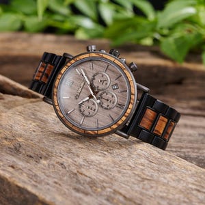 May include: A black and brown wood chronograph wristwatch with a gray face and black hands. The watch has a date window at the 4 o'clock position.