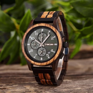 K&ouml;nnte beinhalten: Eine Holzarmbanduhr mit dunkelgr&uuml;nem Zifferblatt und einem Holz- und schwarzen Armband. Das Zifferblatt der Uhr hat silberne Zeiger und Markierungen mit Unterzifferbl&auml;ttern f&uuml;r Sekunden und Minuten. Die Uhr ist mit "VIKING" gekennzeichnet.